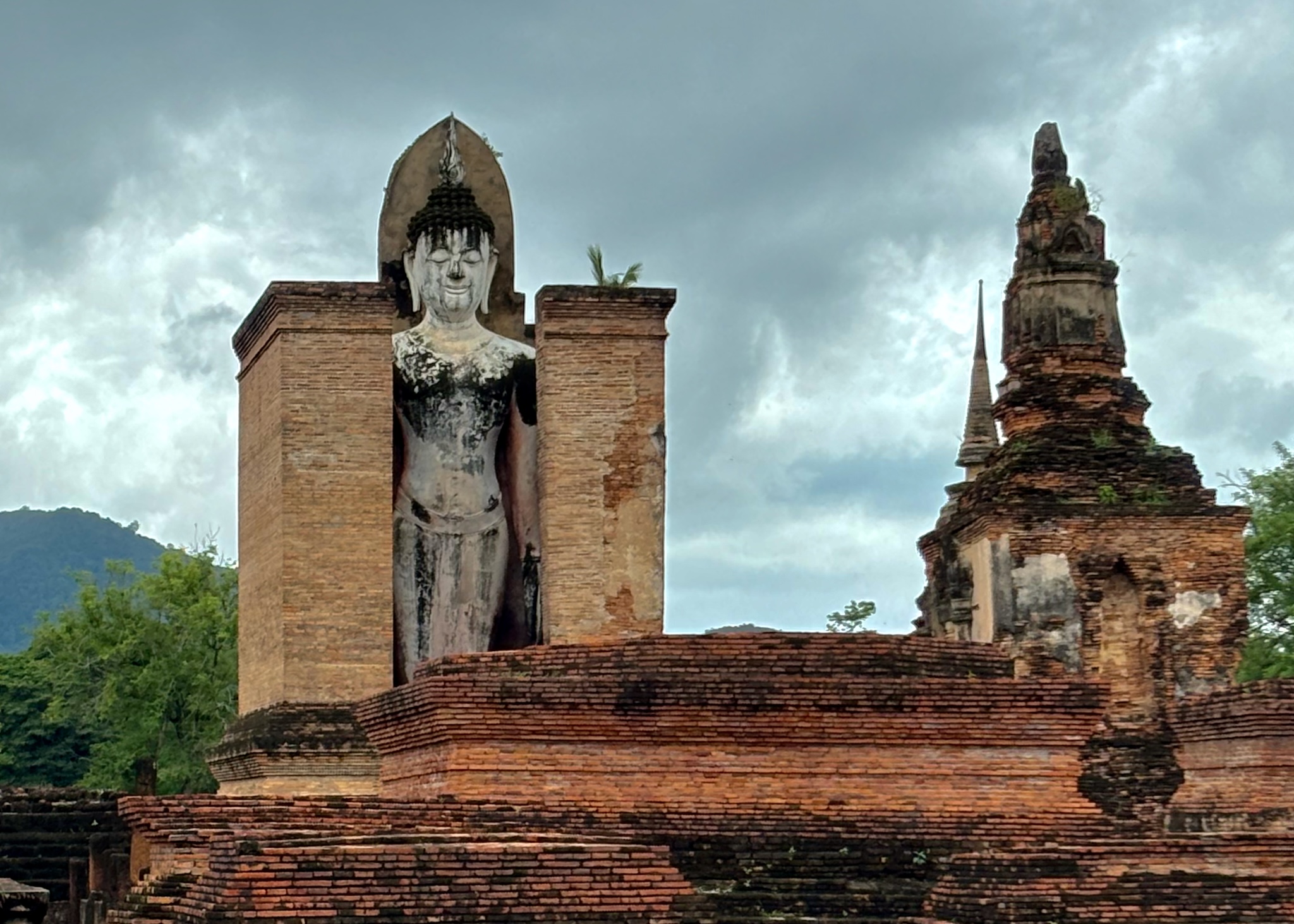 A standing Buddha framed between brick columns under a moody sky at Sukhothai
