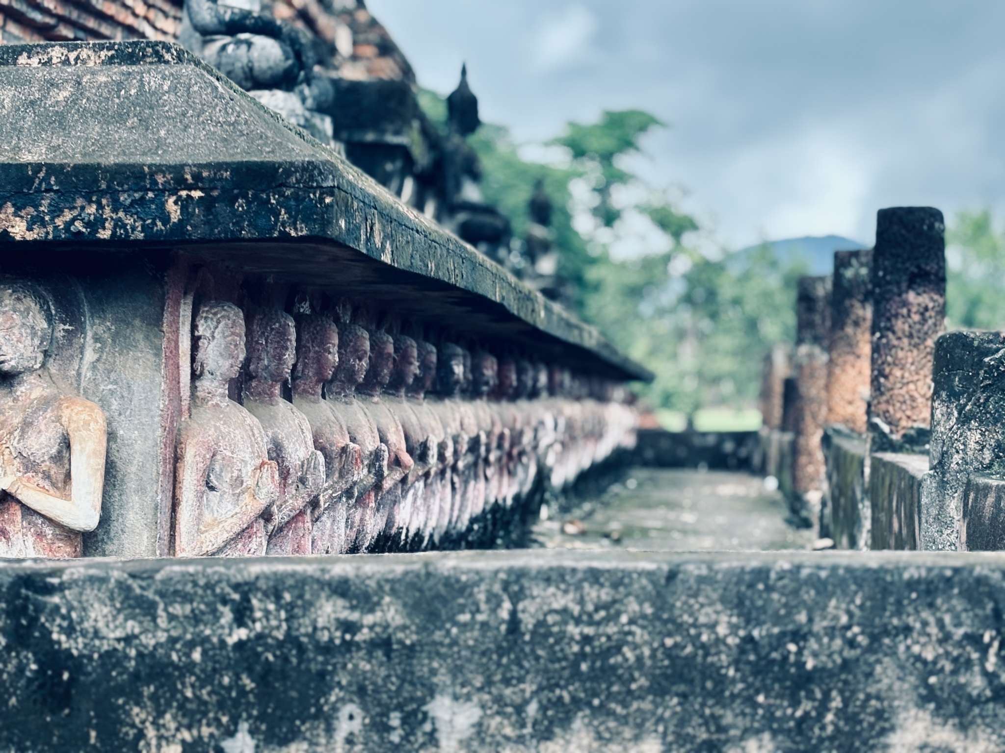A long low row of weathered Buddha reliefs along a temple base at Sukhothai