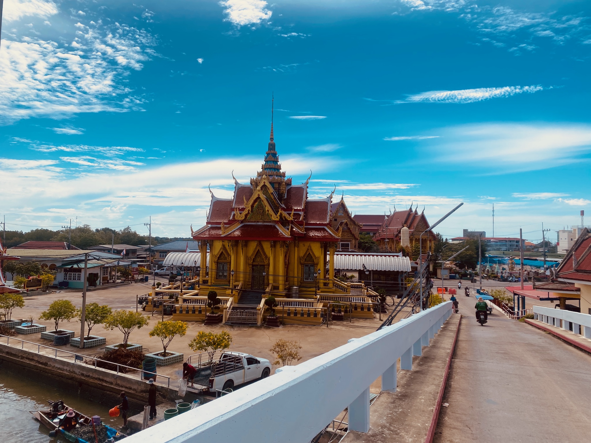 A gilded Thai temple under a wide blue sky, seen from the bridge