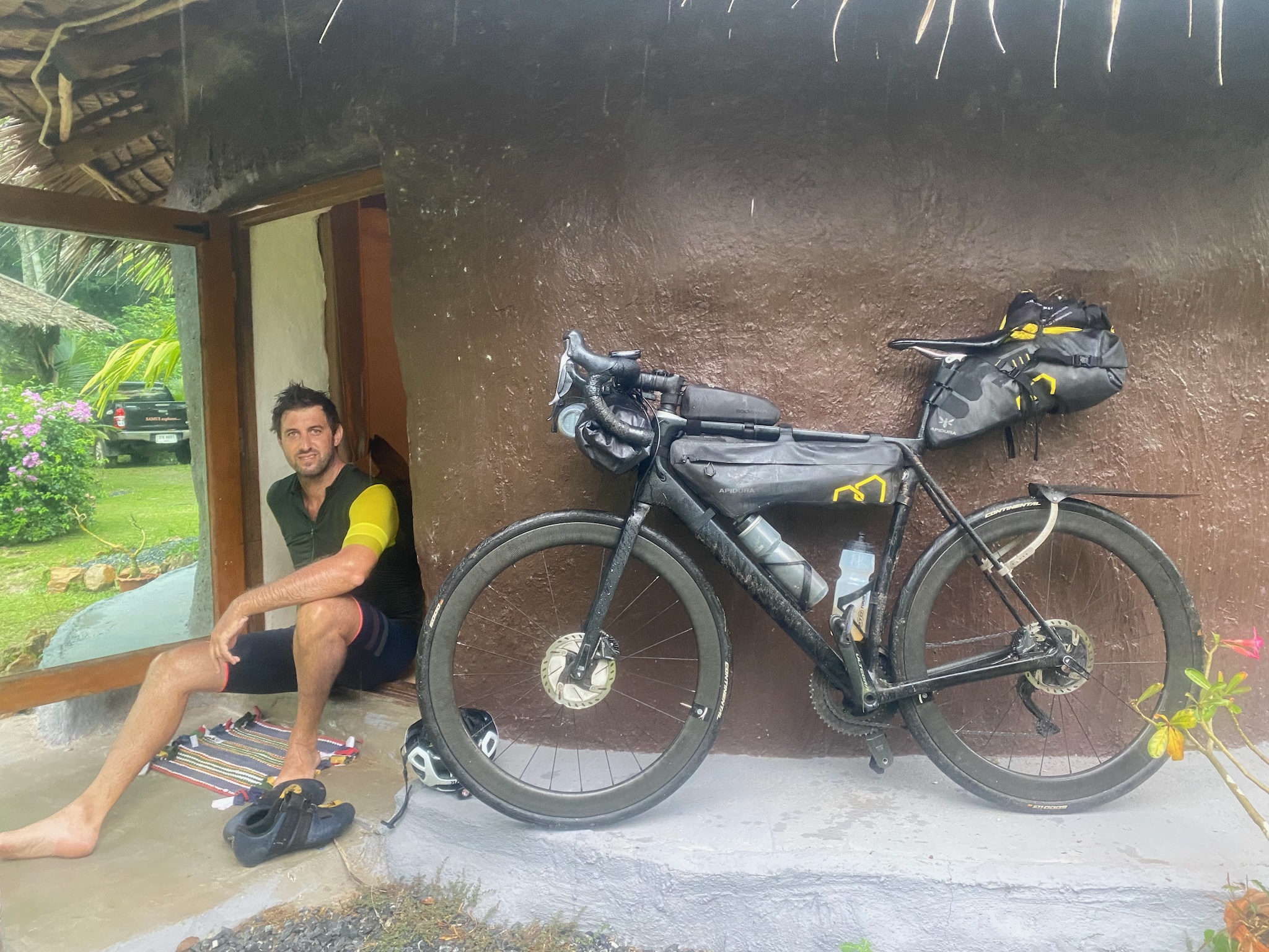 Resting barefoot in the doorway of a mud hut, the loaded bike alongside