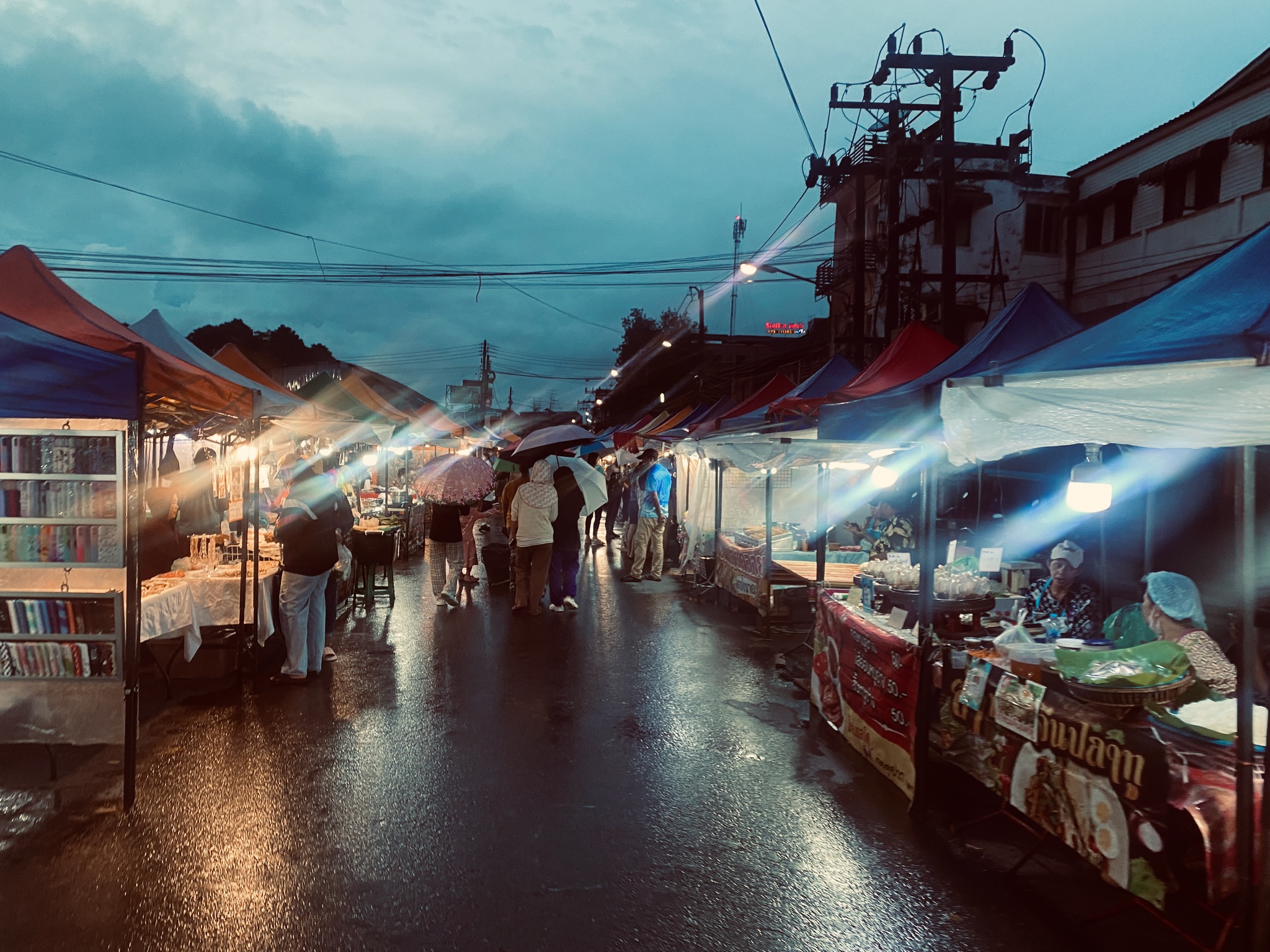 A rainy Thai night market, blue tarpaulins and lamp flare
