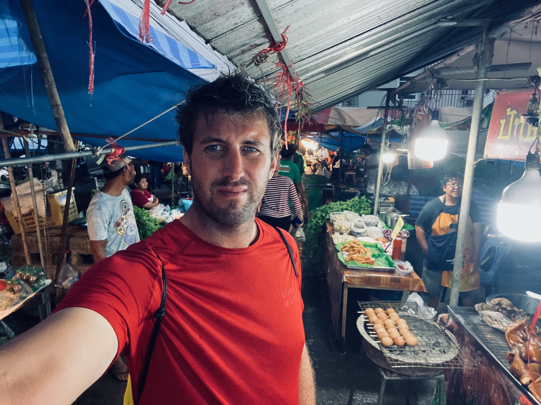 A selfie in a busy covered market, sausages on the grill behind