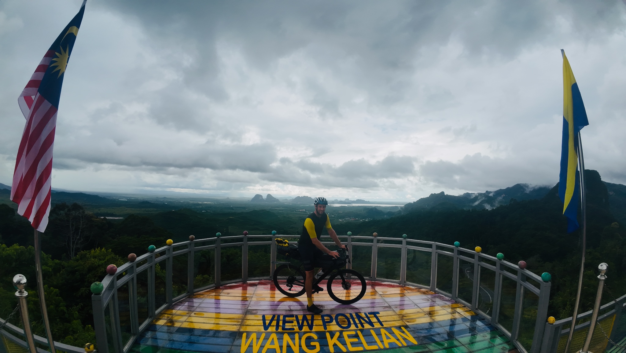 On the rainbow viewing deck at Wang Kelian, Malaysian and state flags flying, karst hills beyond