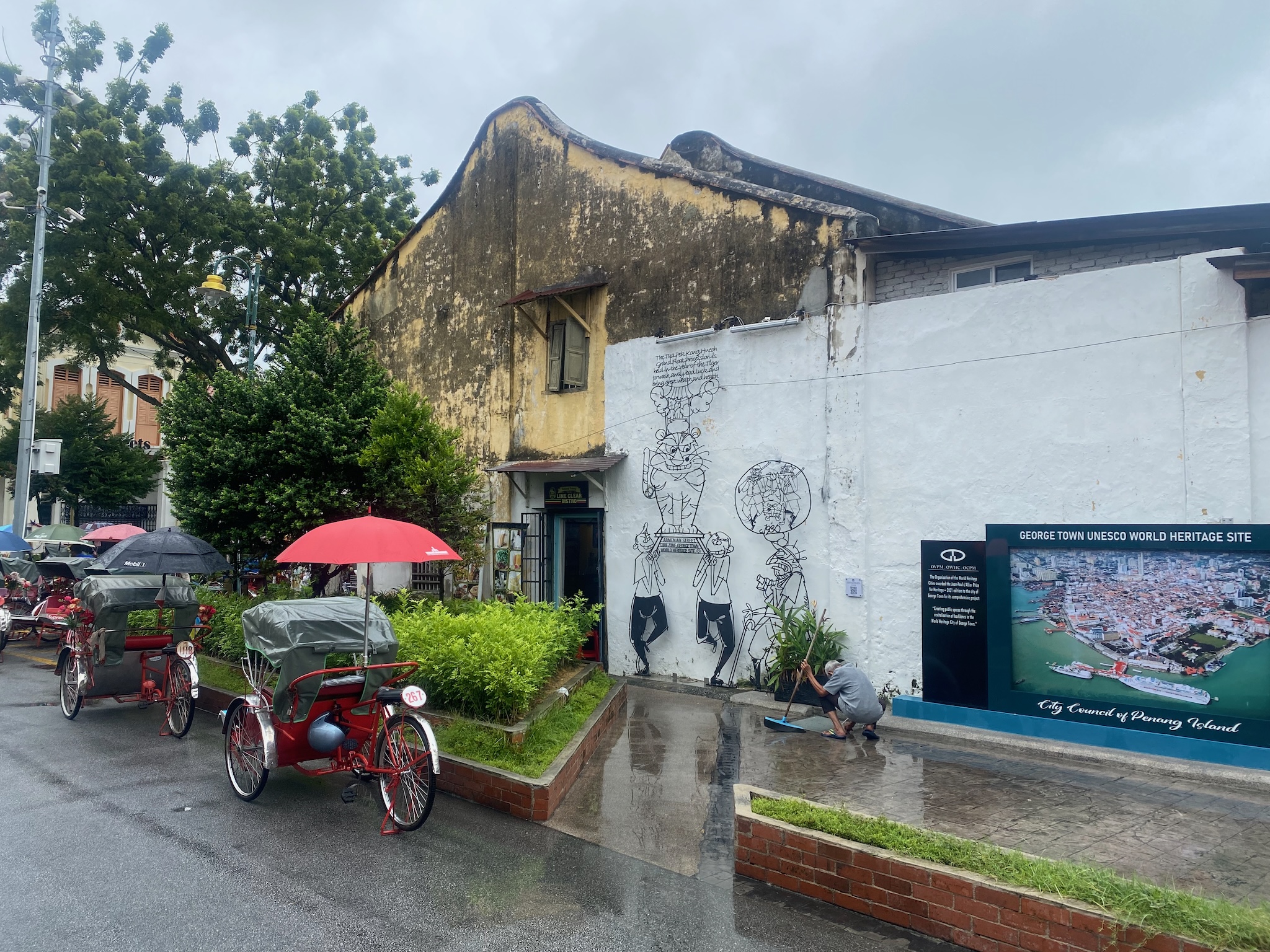 Trishaws and a faded mural in George Town, Penang, in the rain