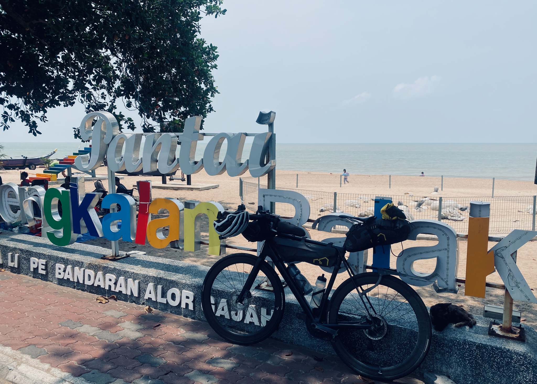 The bike against big colourful Pantai beach letters on the Malaysian coast