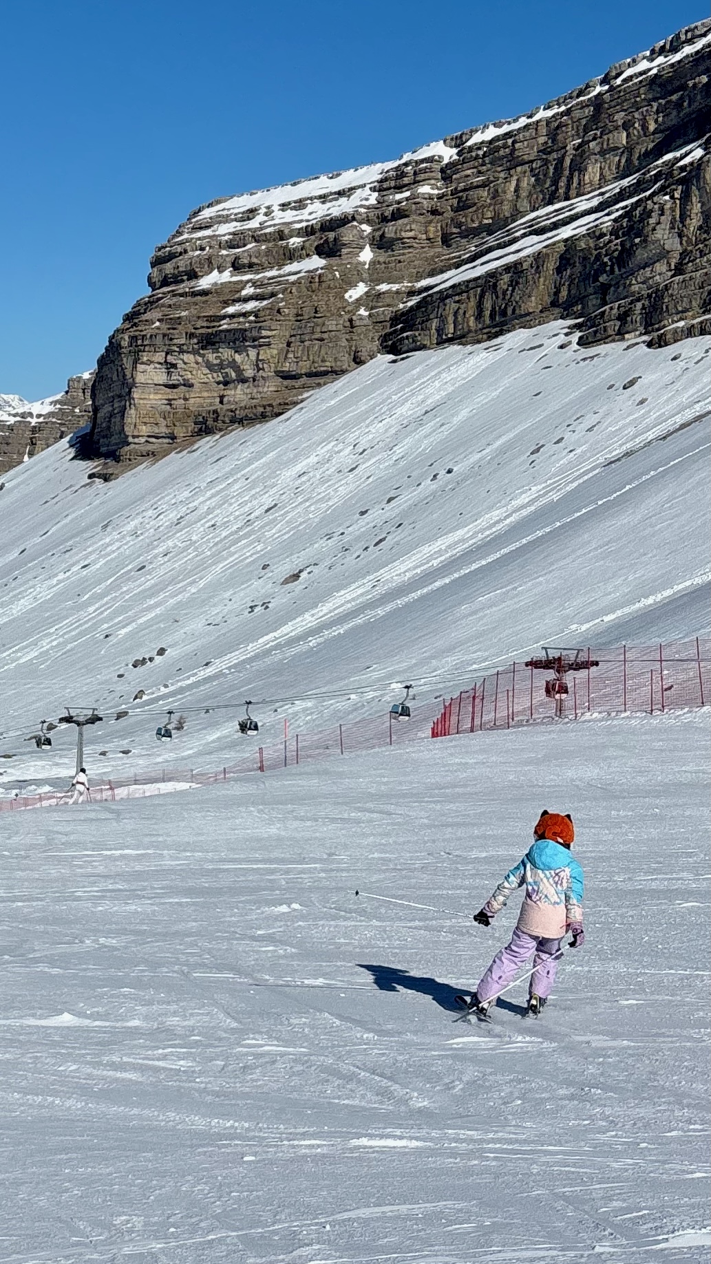 A skier below a big rock cliff and gondola line