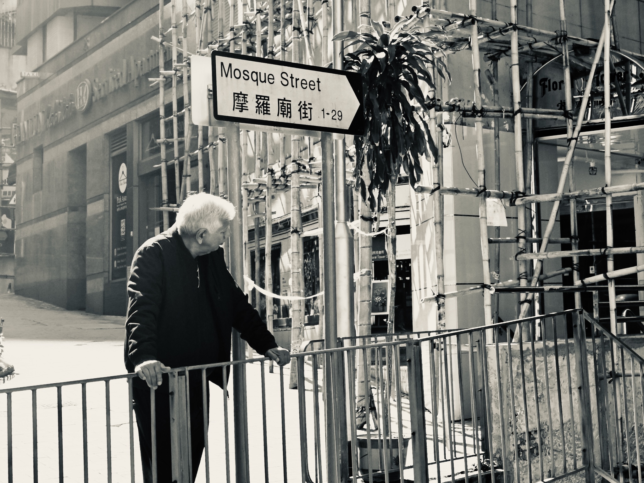An older man at a railing by Mosque Street, black and white