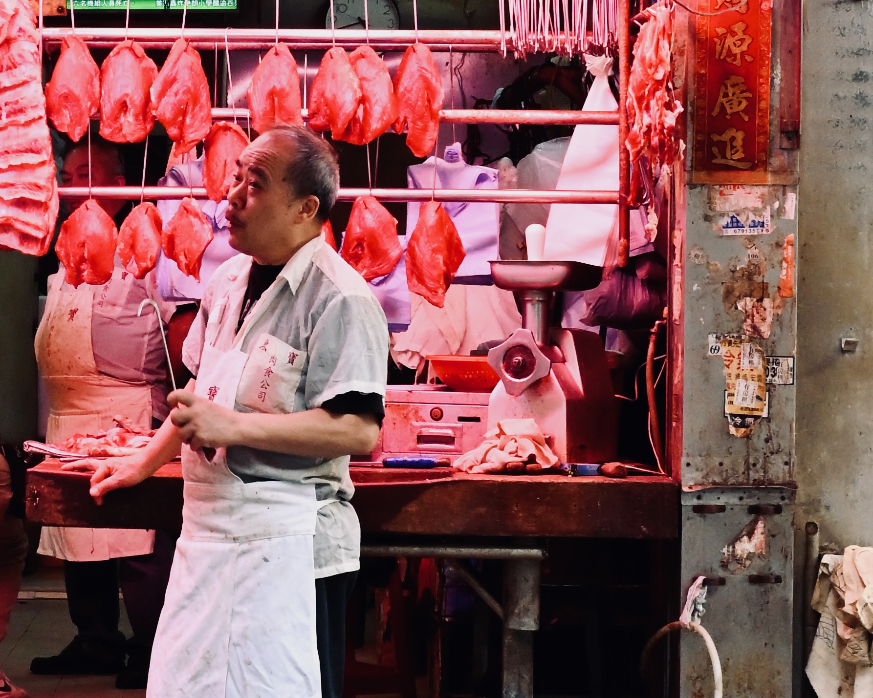 A butcher under hanging meat at a wet market
