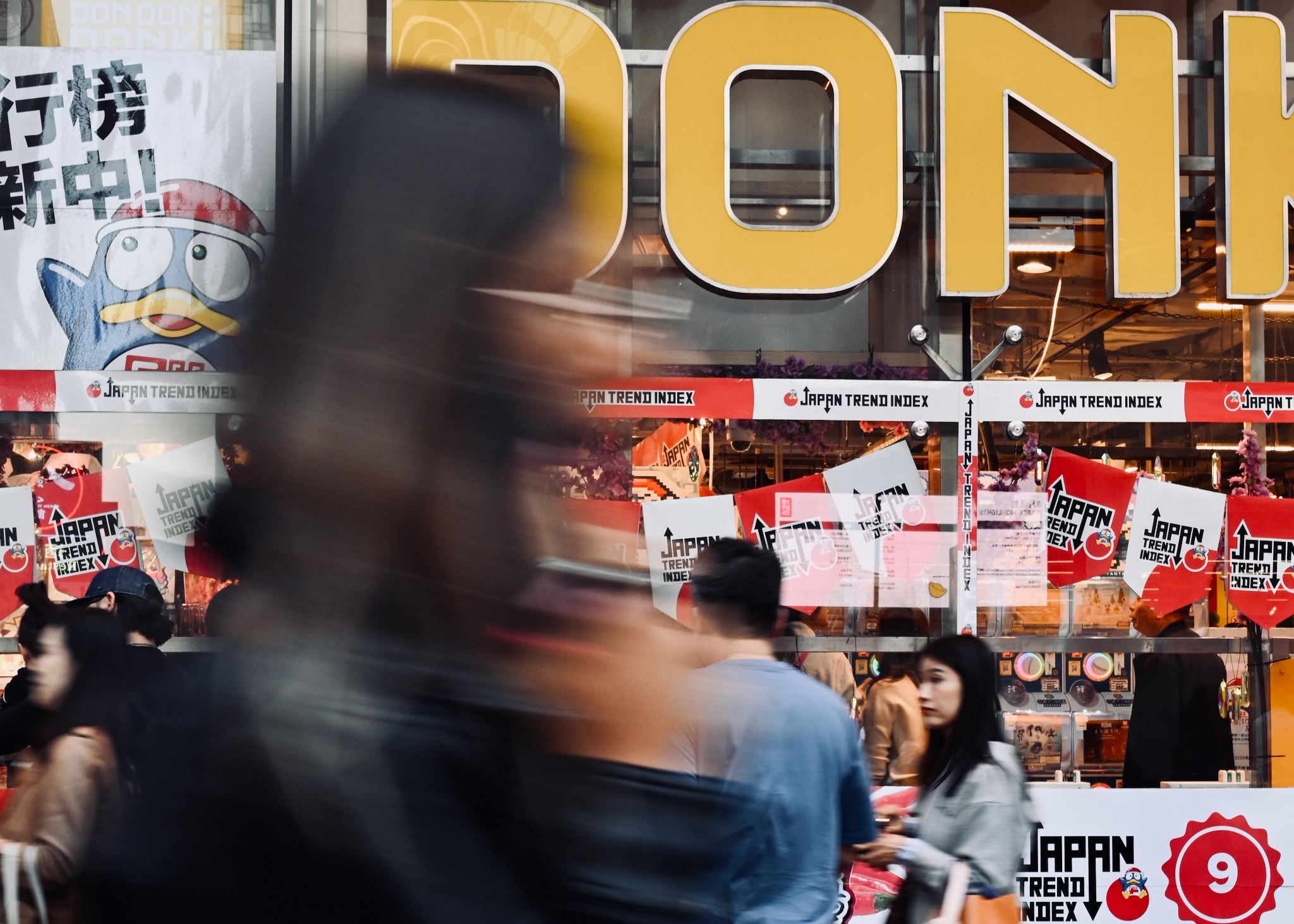 A blurred figure passing a Don Don Donki storefront