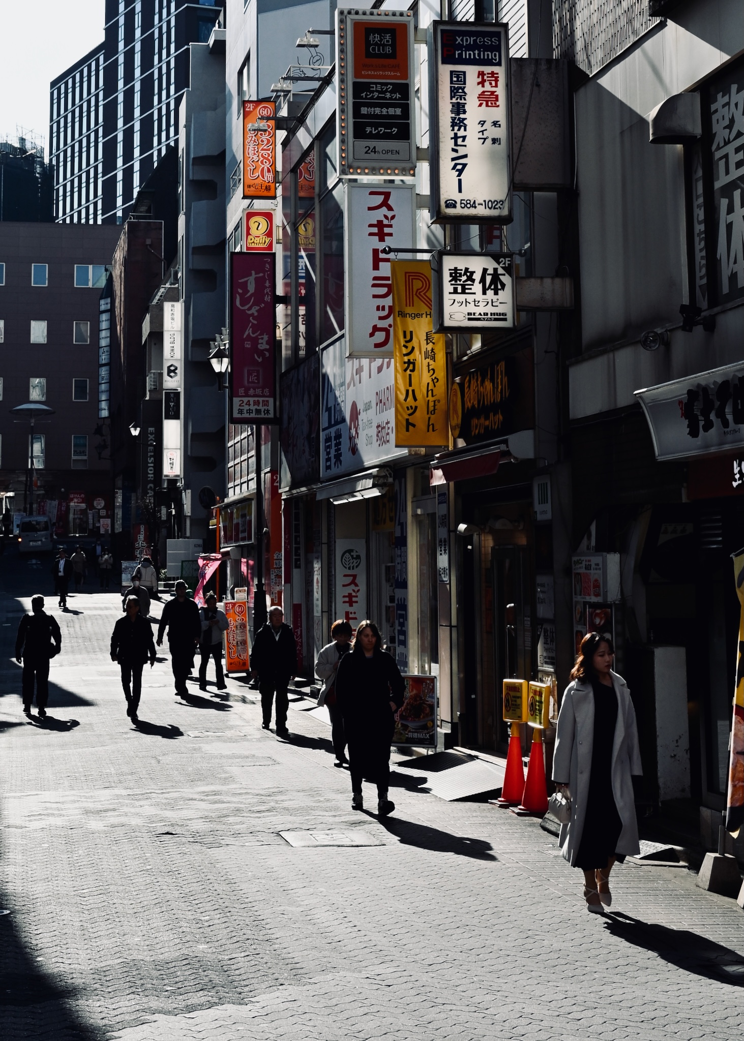 A Tokyo backstreet of signs, a woman in a grey coat walking