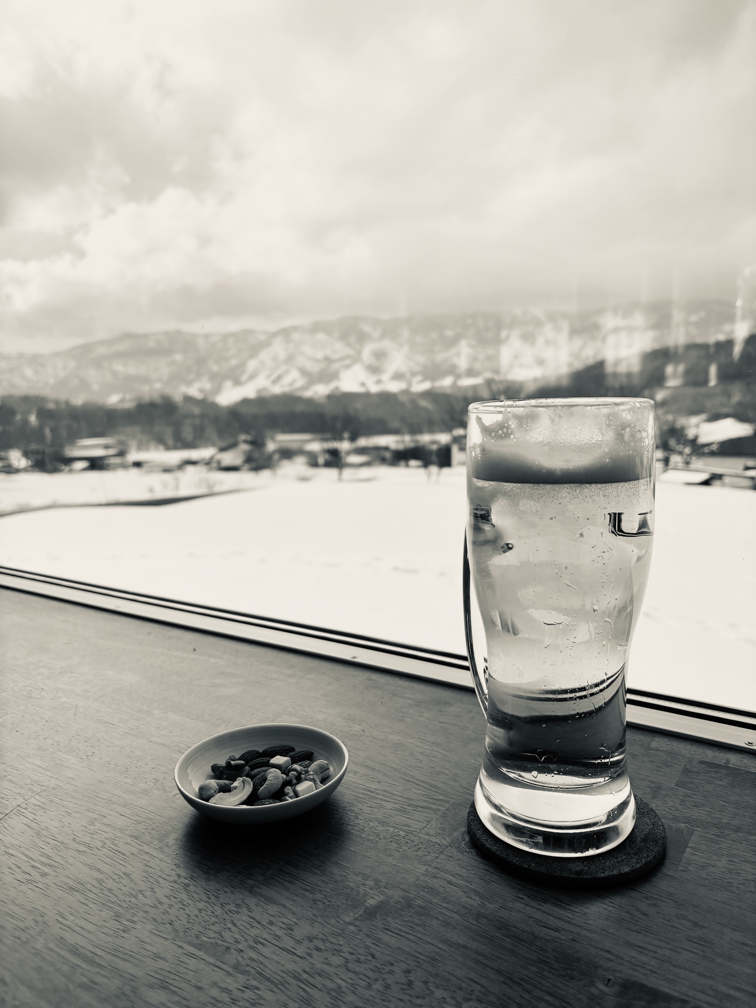 A first beer on the windowsill, snowy mountains beyond, black and white