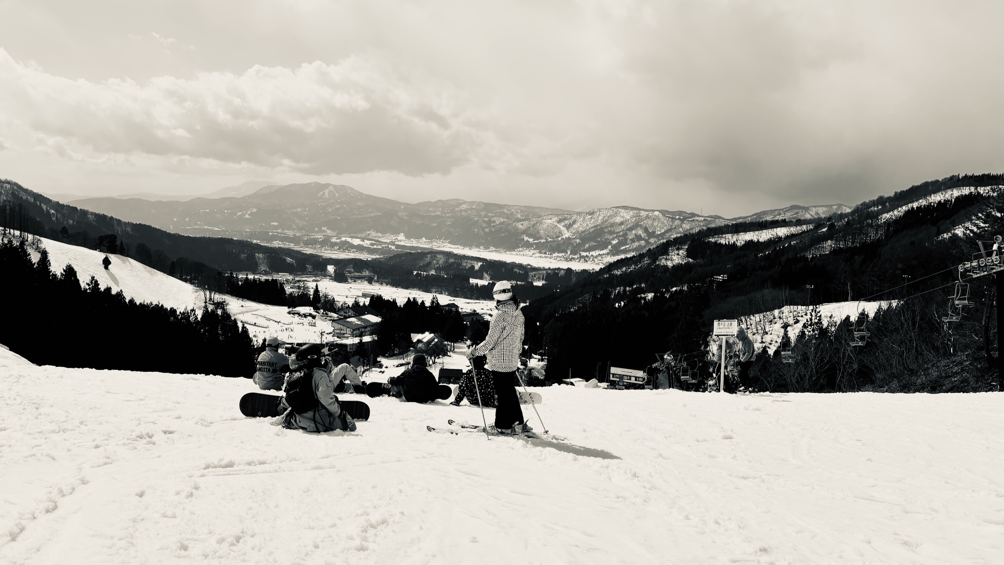Skiers and boarders resting on the slope, looking out over the valley, black and white