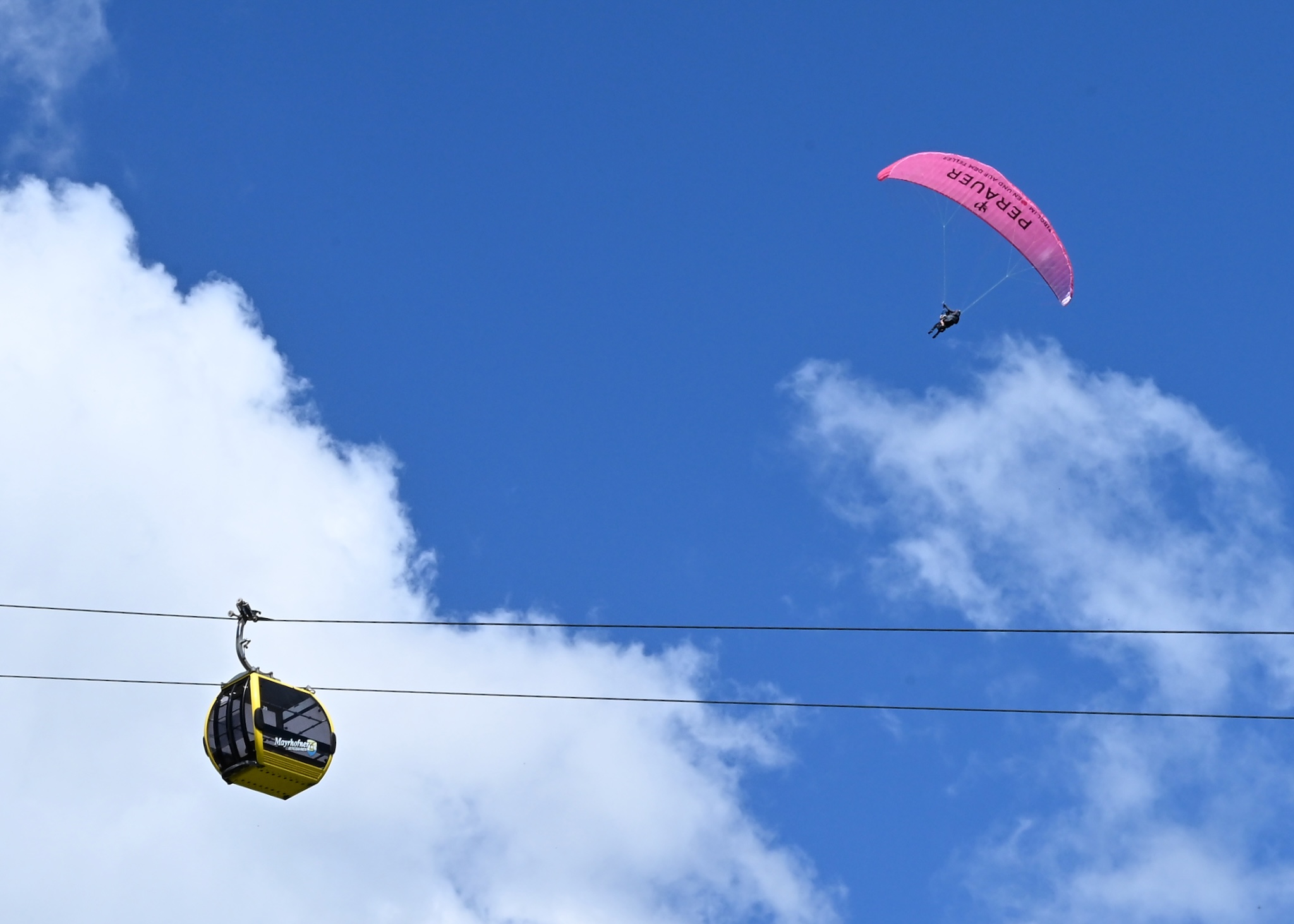 A cable car and a paraglider against blue sky