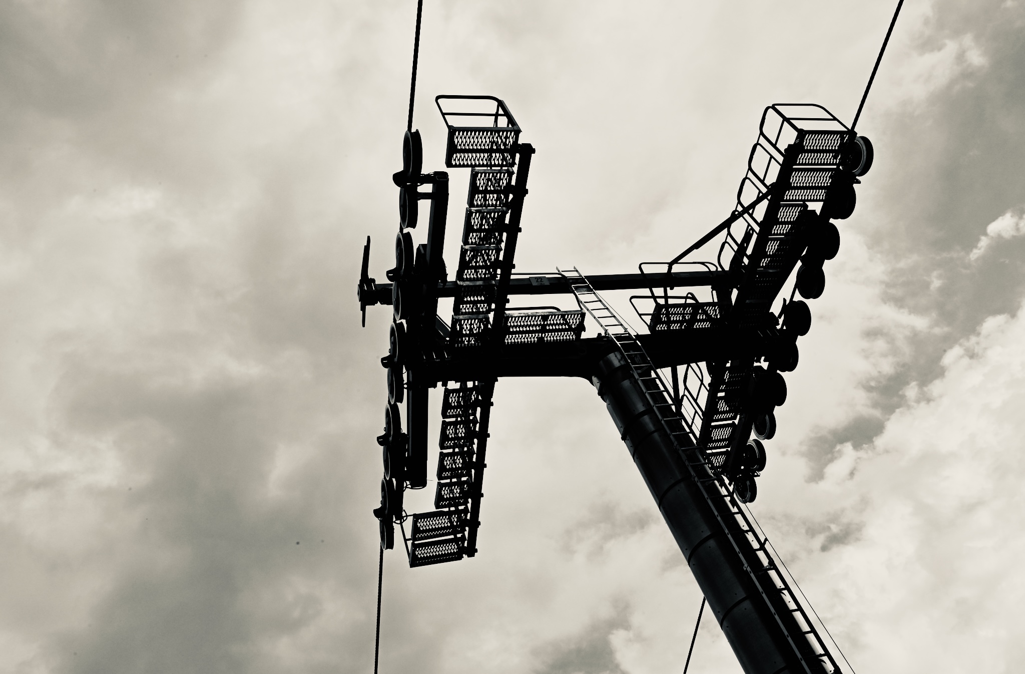 A ski-lift tower in silhouette against cloud, black and white