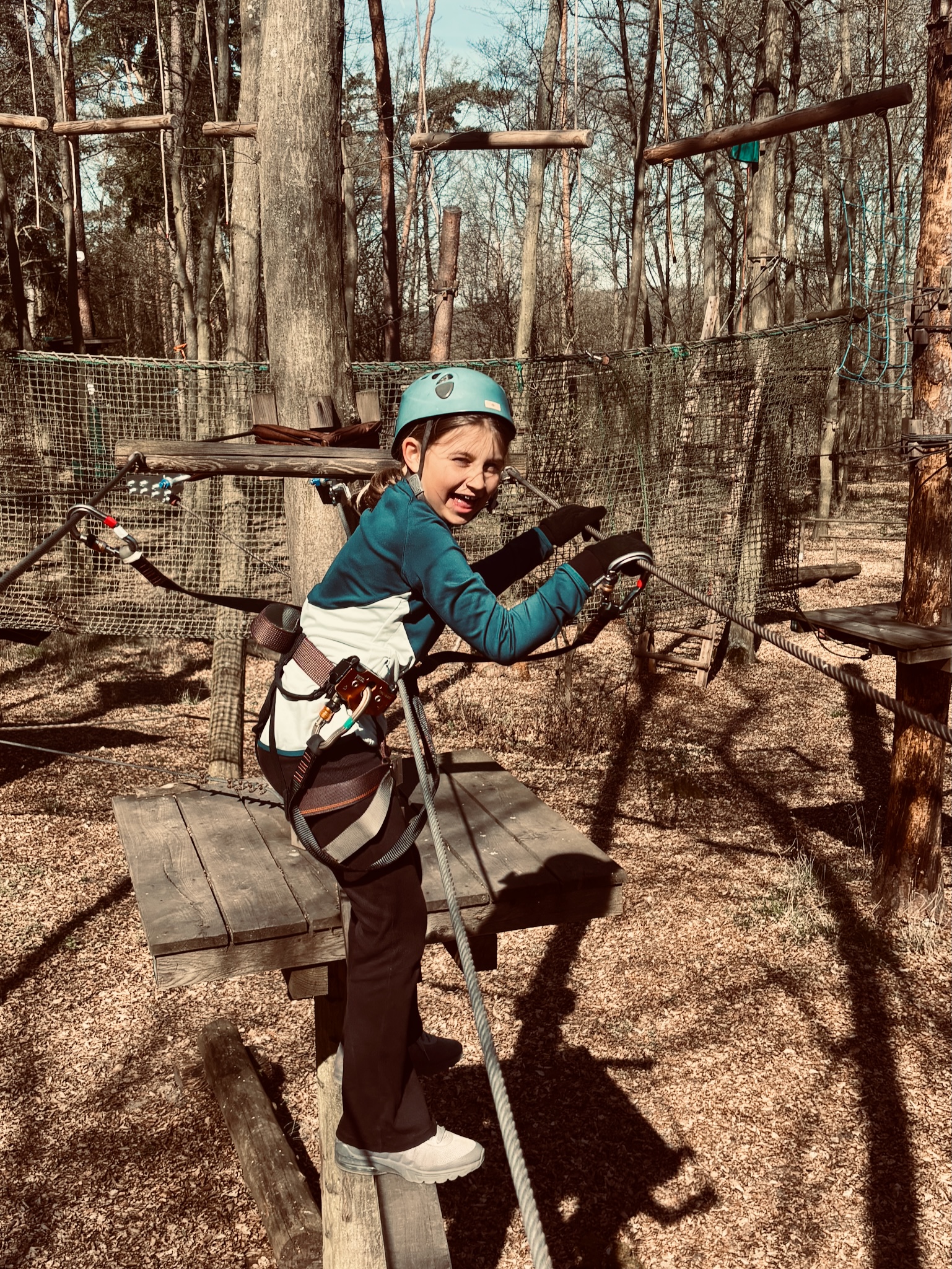 A daughter on the high ropes course in a teal helmet