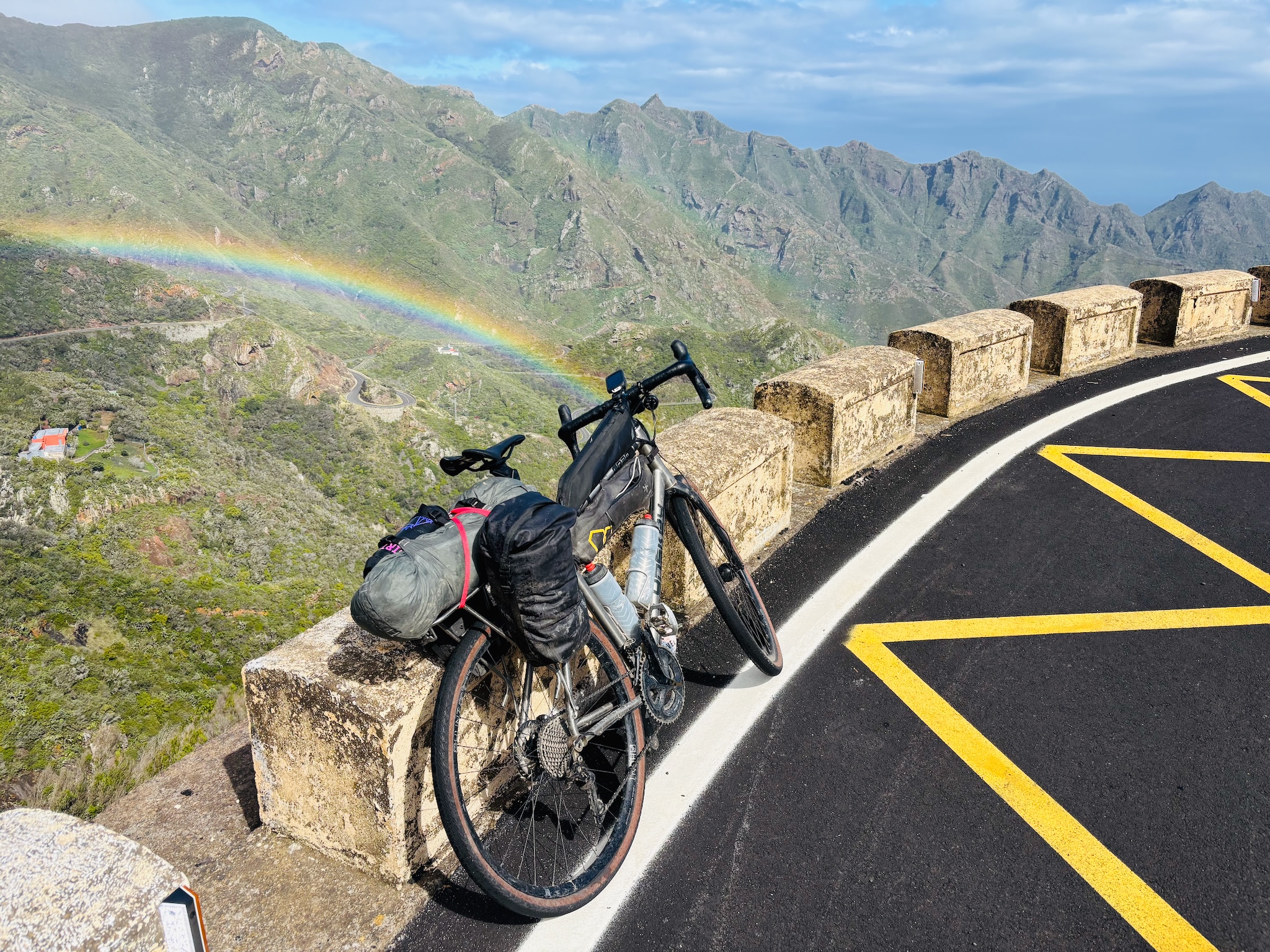 A loaded gravel bike at a mountain viewpoint, a rainbow over the Anaga ridges of Tenerife