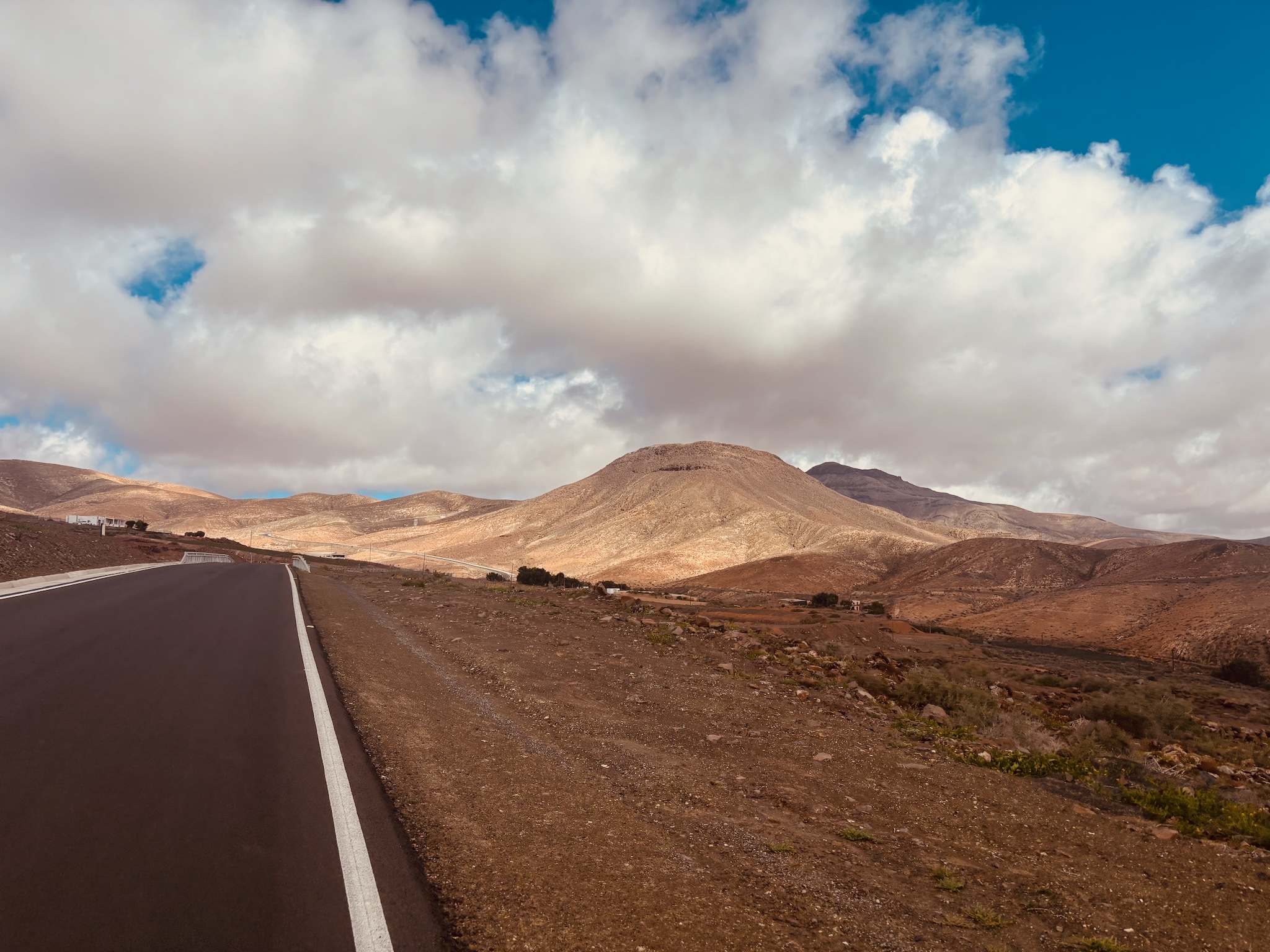 An empty road running into the dry mountains of Fuerteventura under big cloud