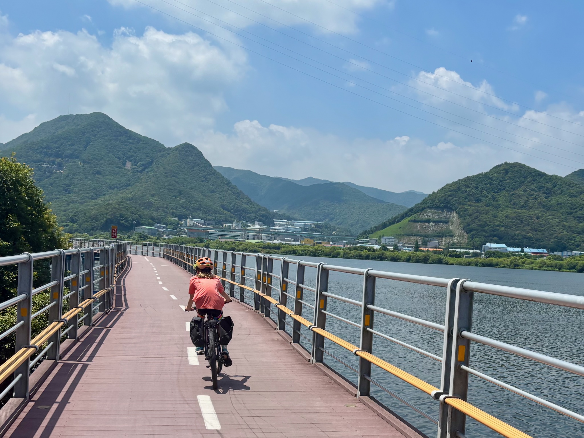 Riding a pink boardwalk above a still lake, mountains beyond