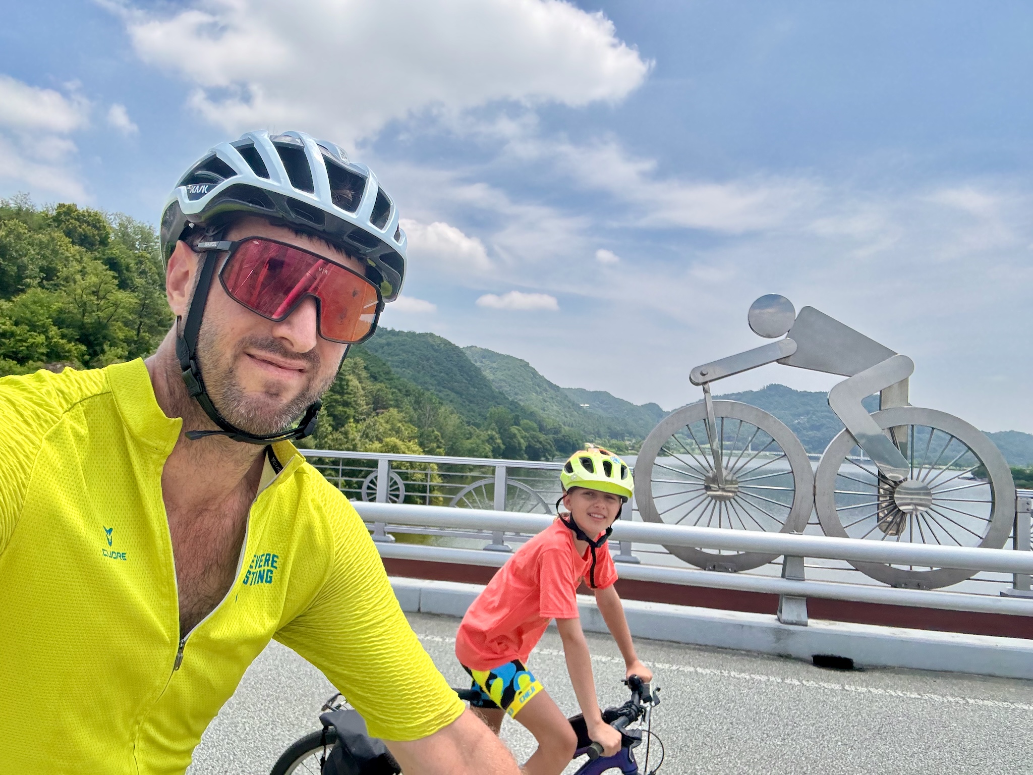 A selfie beside a giant steel bicycle sculpture on a bridge