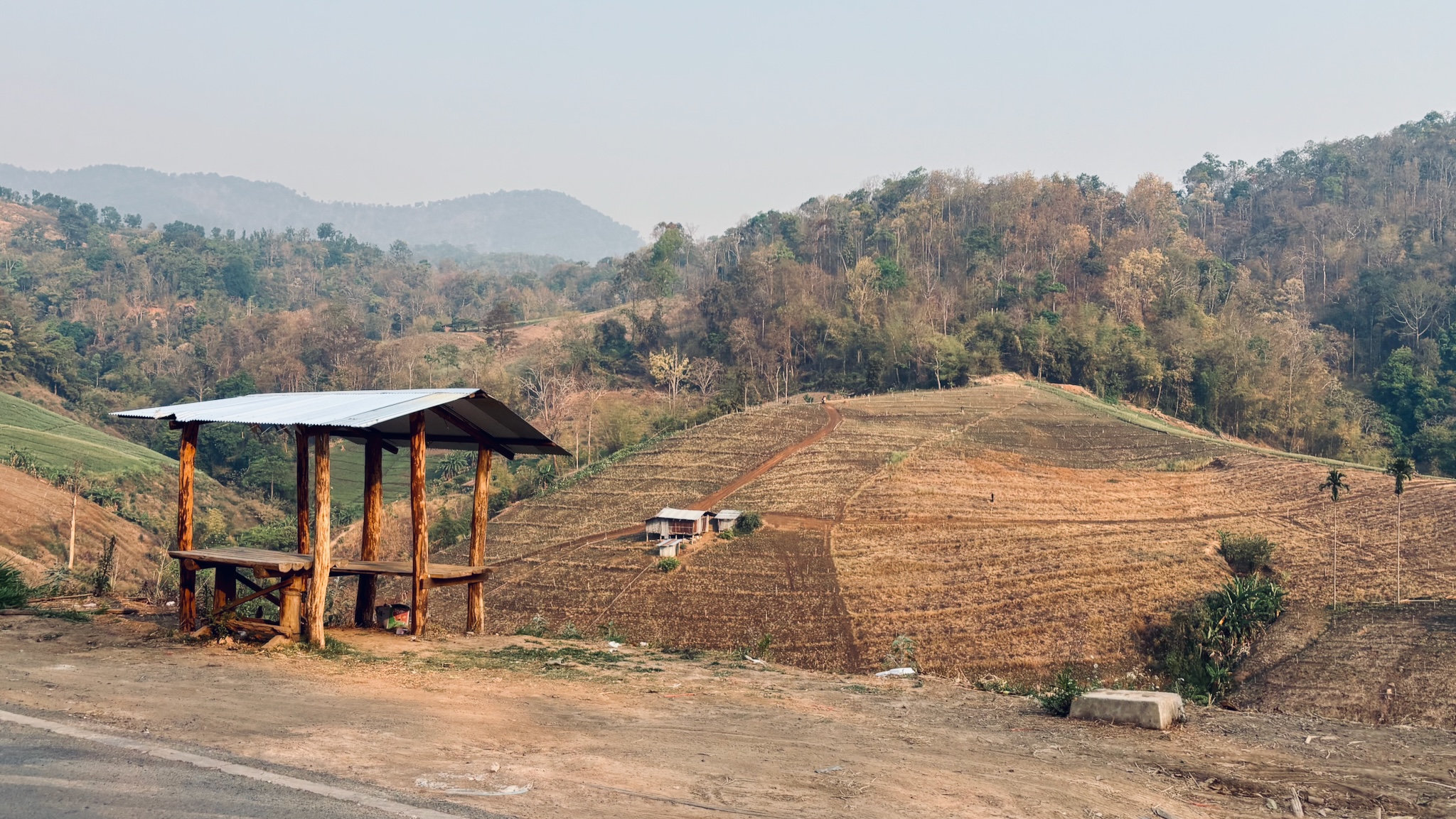 A roadside shelter above terraced fields in hazy dry-season hills