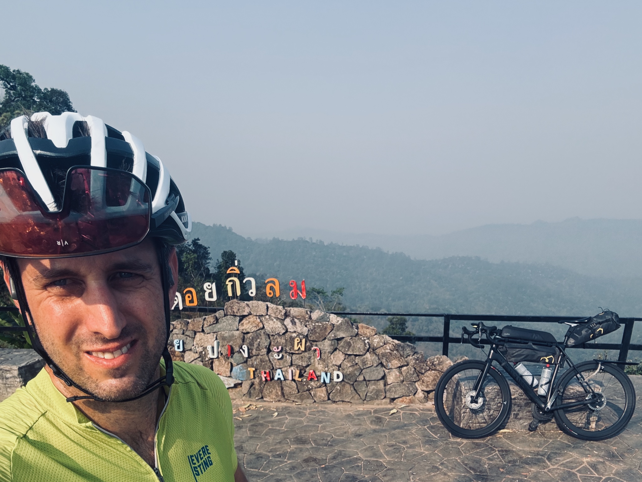Selfie at a stone viewpoint wall reading Thailand, hazy hills beyond