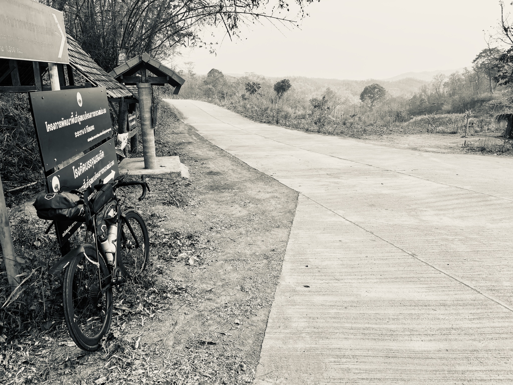 The bike leaned by a project sign on an empty concrete hill road, in black and white